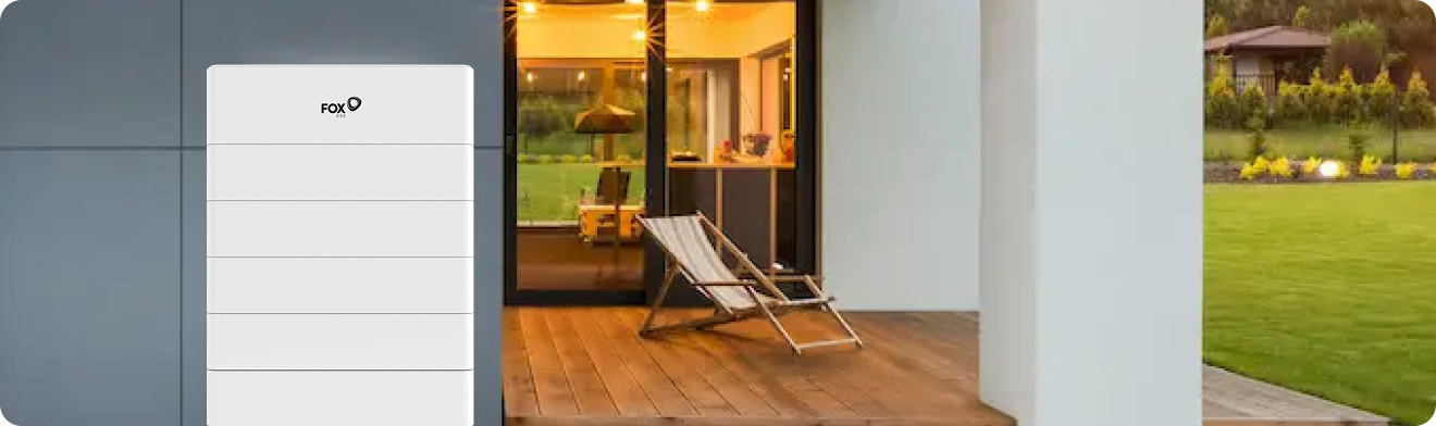 A FOX brand home battery unit installed on the exterior of a modern house with a comfortable well-lit patio
